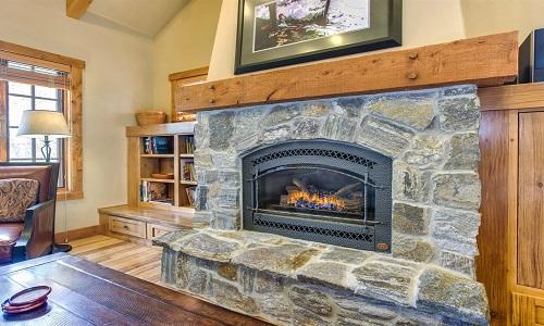 A stone hearth houses a propane fireplace, providing a warm focal point. Above the mantel, a framed artwork adds character. Wooden cabinetry and bookshelves are visible on either side, creating a cozy and inviting atmosphere in the living space.