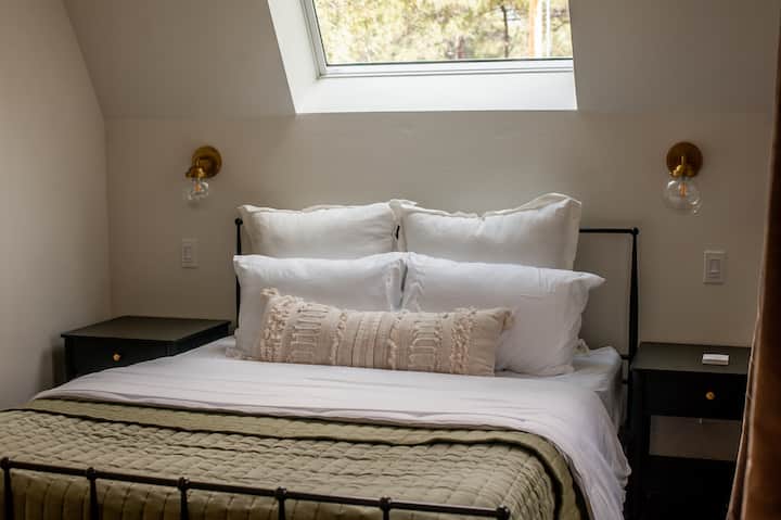 Cozy skylit bedroom with plush linens, modern sconces, and nightstands