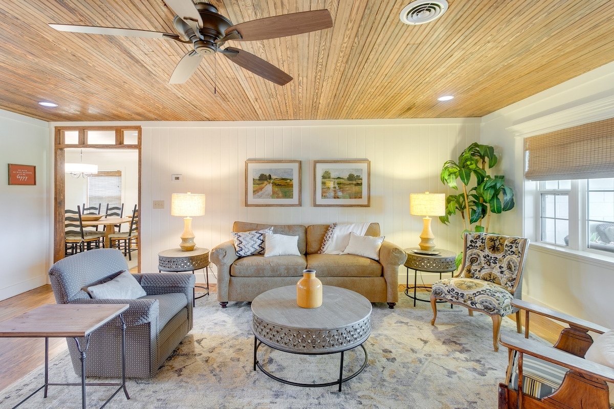 A welcoming living area features a light-colored sofa paired with an accent chair and a cozy armchair. Natural light enters through the window treatments, illuminating the textured ceiling and stylish decor. A round coffee table centers the space, enhancing the comfortable atmosphere.