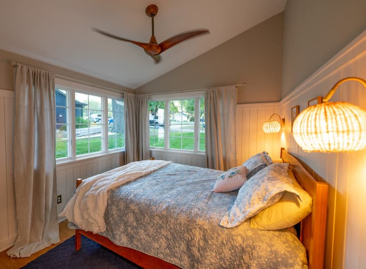 Მშვიდი საძინებელი კუთხის ფანჯრებით, რბილი განათებითა და თეთრეულით - იდეალურია მშვიდი ტბისპირა დილისთვის.