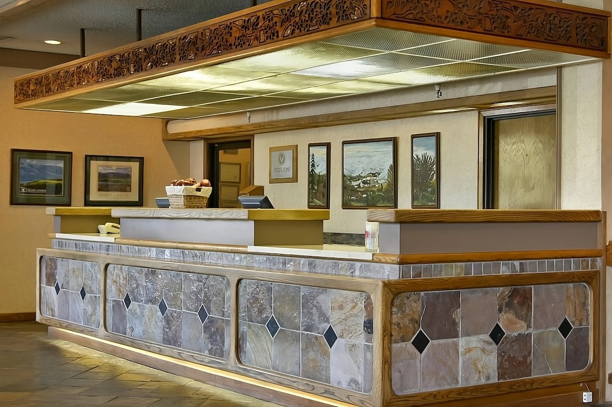 The front desk area is showcased, featuring a stone-tiled counter with decorative accents. Art displayed on the wall adds character, while a basket of snacks is presented on the counter, inviting guests to feel welcomed upon arrival.