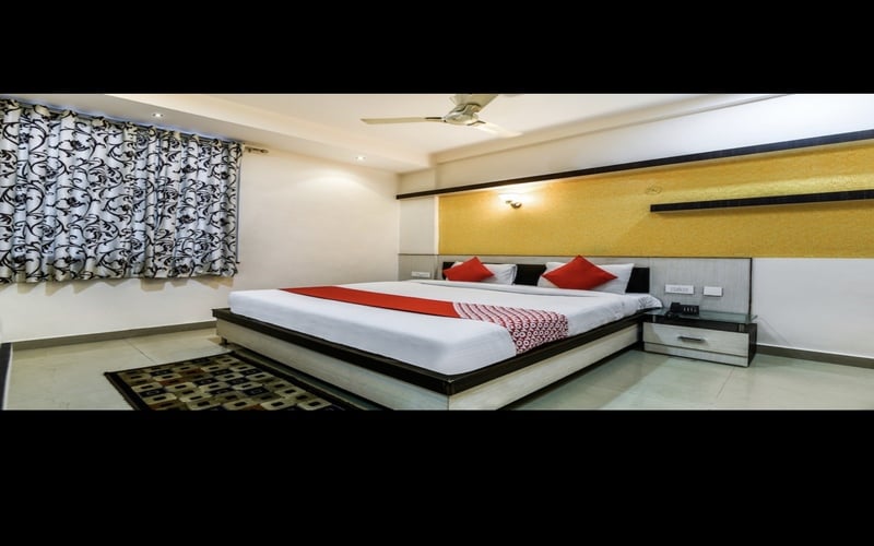 A well-appointed bedroom features a spacious bed adorned with red accent pillows. The walls are complemented by a patterned curtain and a decorative gold panel. A bedside table provides additional function, while a ceiling fan contributes to the room's modern design.