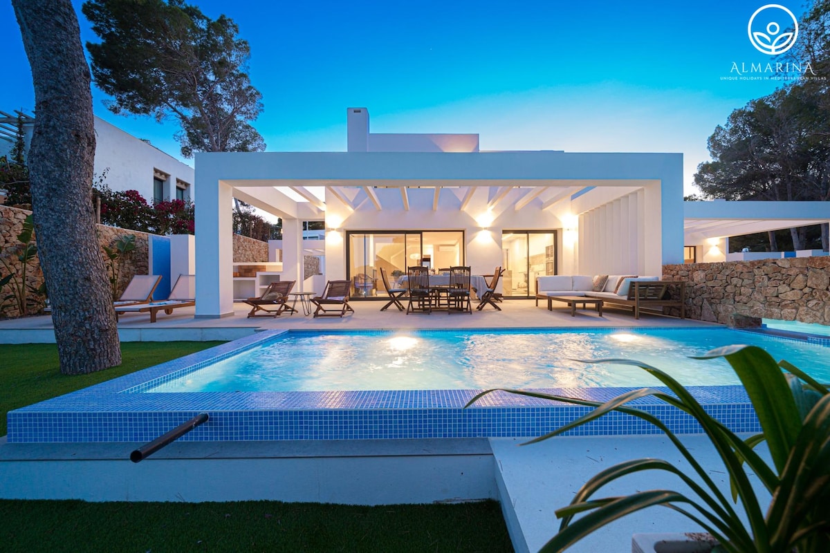 A modern villa is depicted with a swimming pool in the foreground and a spacious terrace area featuring lounge chairs and a dining set. Large glass doors provide access to the interior, while well-maintained greenery surrounds the property, complementing the tranquil atmosphere.