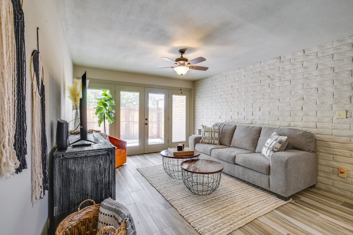 A comfortable living area features a light grey sectional sofa and a rustic wooden coffee table. Natural light streams in through glass doors leading to a patio, while textured walls add depth to the space. A TV and decorative elements complement the inviting atmosphere.