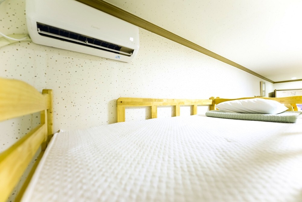 A well-structured bunk bed is depicted, featuring a clean mattress covered with fresh bedding. A pillow rests neatly on top of the bedding. The room includes an air conditioning unit mounted on the wall, contributing to a comfortable indoor environment.