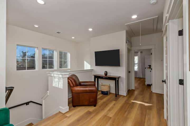 Lofti në krye të shkallëve ka një televizor inteligjent 55", karrige të lehtë dhe divan futon kadifeje