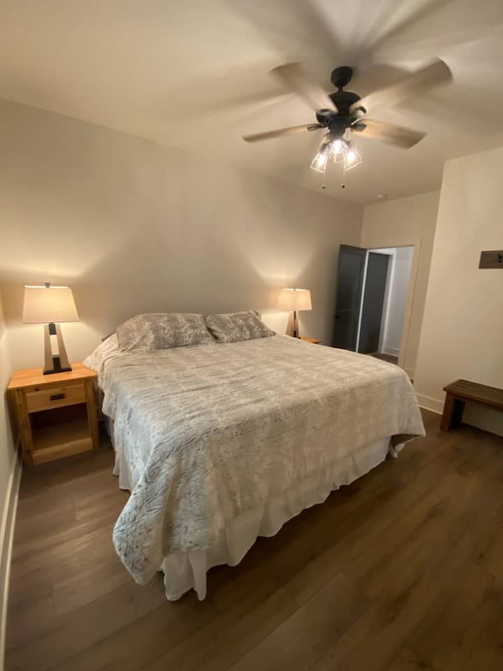 Cama tamaño king con televisor y ventilador de techo en la habitación y baño adjunto