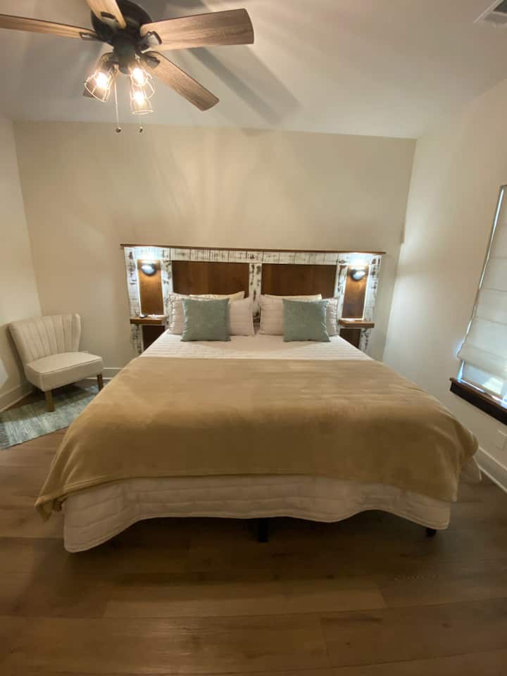 Cama tamaño king con TV montada y ventilador de techo en la habitación y baño privado.