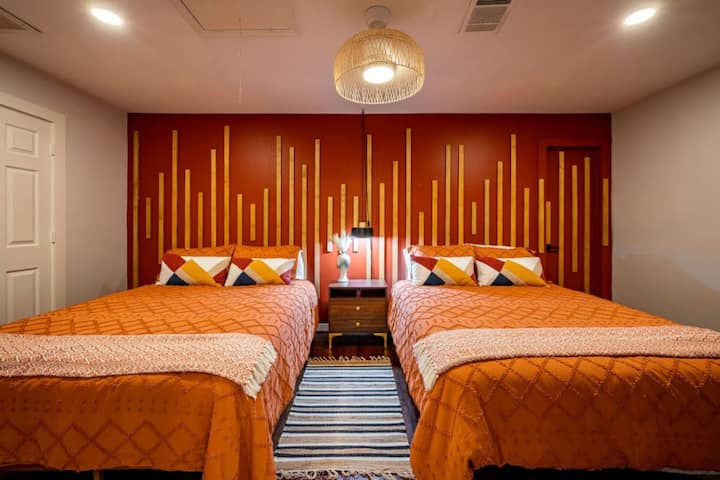 Vibrant double-bed room with bold accent wall, cozy linens, and playful color-block pillows—perfect for groups or families.