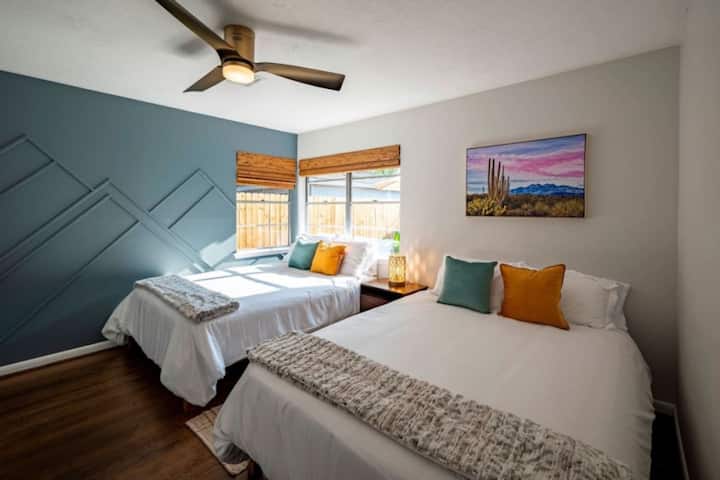 Sunlit bedroom with two double beds, colorful pillows, and modern accent wall—bright, cozy, and perfect for sharing.