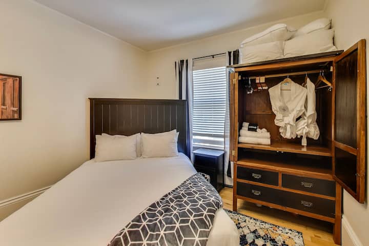 Dhoma blu ka një pamje nga rruga Noe së bashku me një gardërobë për të shpaketuar, një tavolinë pune dhe një karrige.