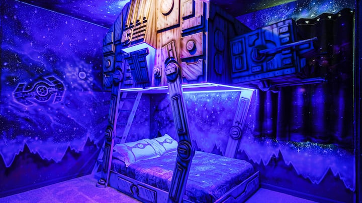 Habitación épica con temática de Star Wars con litera AT-AT, murales galácticos e iluminación LED brillante.