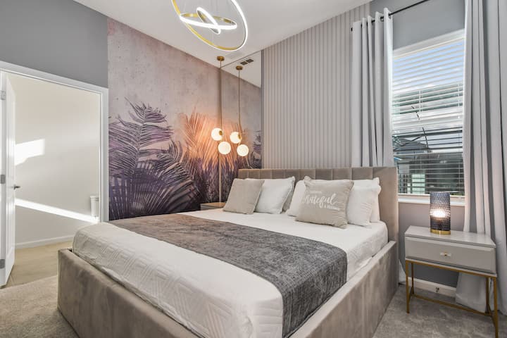 Chumba cha kulala cha kisasa chenye rangi laini, mitende na mwangaza wa kifahari kwa ajili ya mapumziko.