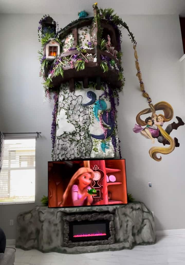 Step into a fairytale! This Rapunzel-inspired living room features a soaring tower, whimsical wall art, a large 75” Smart TV, and a cozy electric fireplace.