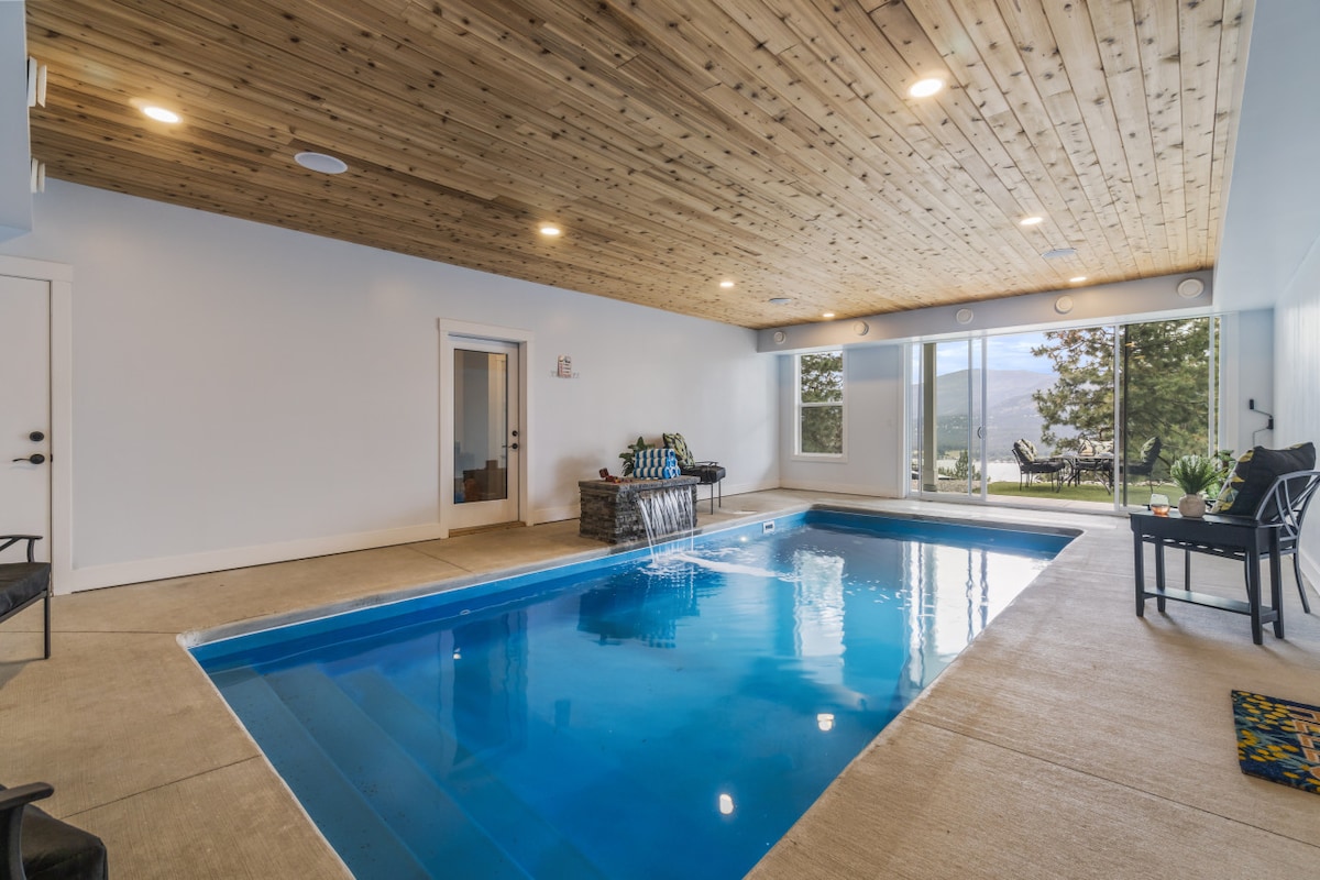 An indoor private pool is showcased under a wooden ceiling, enhancing the sense of spaciousness. Natural light pours in through large windows, reflecting off the clear water. A seating area with plush chairs is positioned nearby, providing a perfect spot for relaxation.