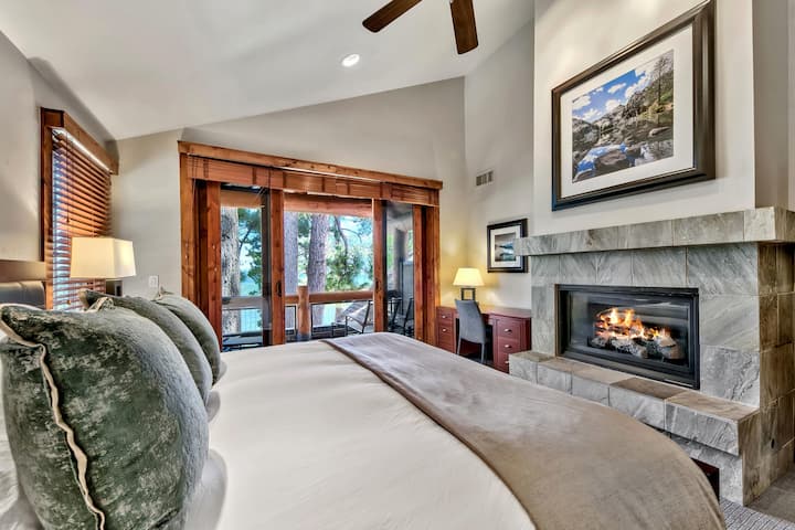 Bedroom features a stone-tiled fireplace, wood-trimmed sliding doors to balcony, and a wooden desk with lamp.