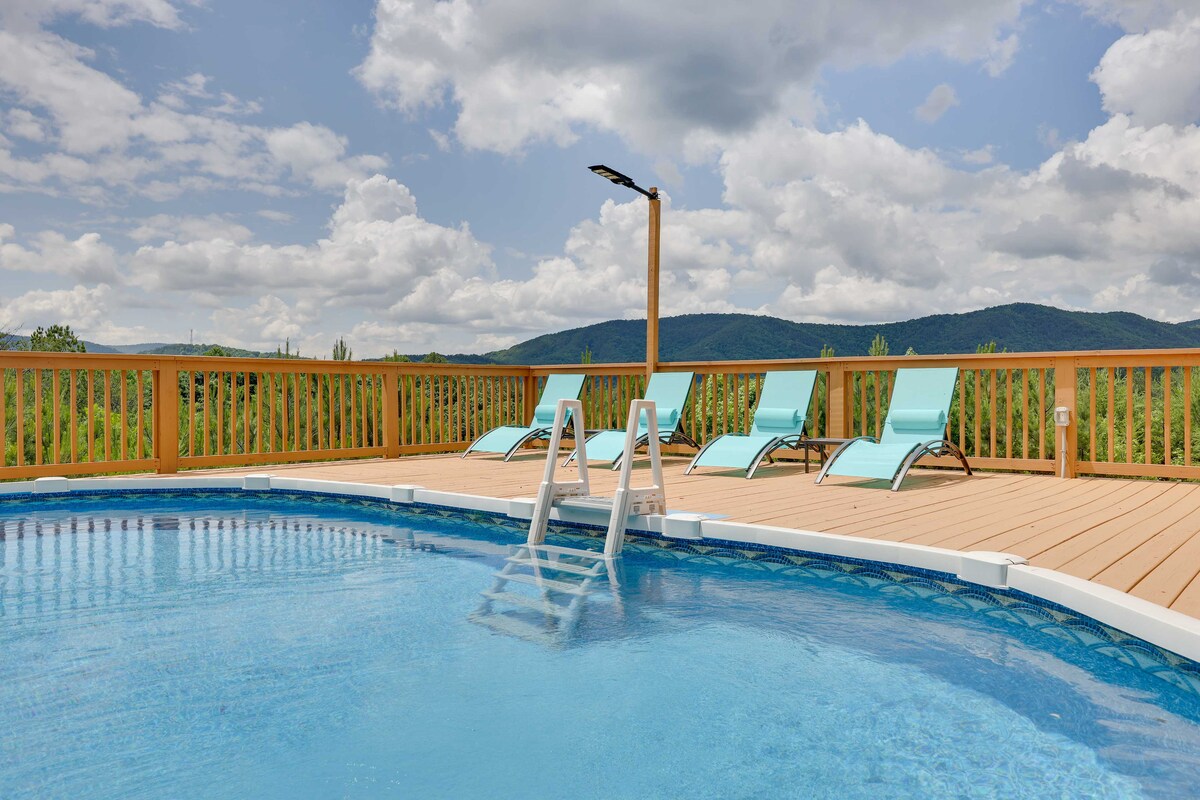A private saltwater pool is surrounded by a wooden deck, featuring three light blue lounge chairs positioned for mountain views. Lush greenery and rolling hills stretch into the distance under a partly cloudy sky, creating a serene outdoor space.