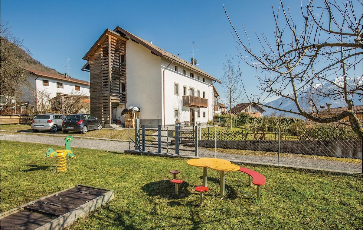 A charming exterior of a renovated house is presented, featuring balconies and wooden accents. In the foreground, a well-maintained garden area includes colorful play structures and seating, surrounded by greenery, providing a welcoming space for children and relaxation.