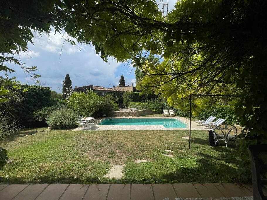 A serene outdoor area is highlighted by a private swimming pool surrounded by lush greenery. Sun loungers are positioned nearby, and a variety of shrubs and plants create a natural barrier, enhancing the tranquil garden atmosphere.
