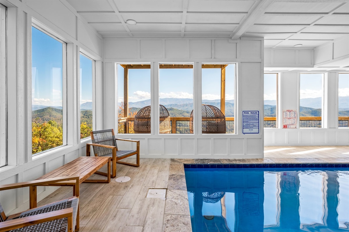 An indoor pool area is highlighted, featuring large windows that showcase panoramic mountain views. Natural light floods the space, illuminating the pool and surrounding wooden seating. The atmosphere is tranquil, with the scenic backdrop enhancing the overall appeal of the indoor setting.