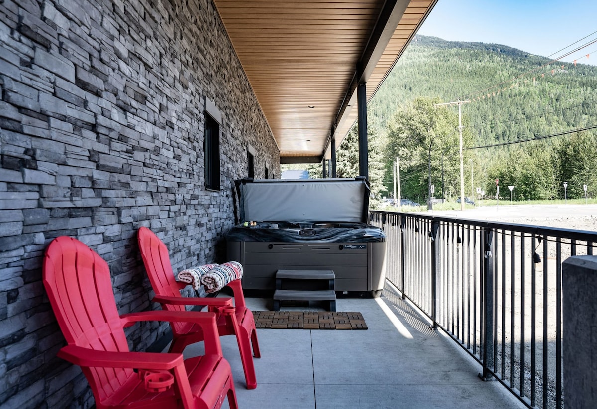 A private patio is equipped with two red Adirondack chairs and a hot tub. The patio area features stone walls and a view of the surrounding natural landscape, enhancing outdoor relaxation and enjoyment.