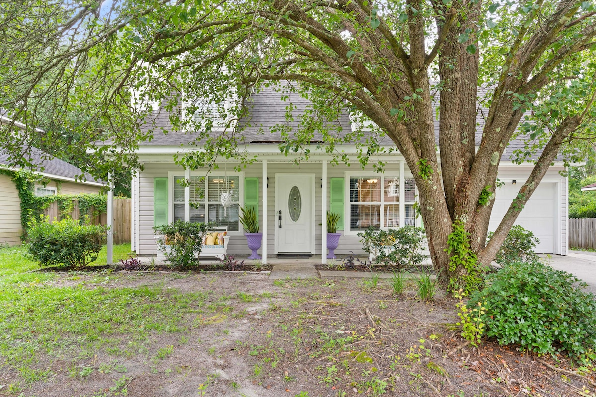 The exterior of the home features a welcoming front porch with comfortable seating, flanked by vibrant planters. A large tree provides shade, and the lush green landscaping enhances the inviting curb appeal of the house.