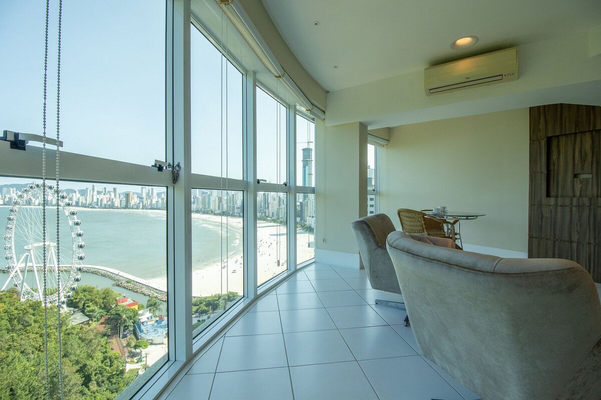A bright living room showcases large floor-to-ceiling windows, offering a panoramic view of the beach and the Ferris wheel. Comfortable seating is positioned to take in the scenery, while the clean decor enhances the open, airy feel of the space.