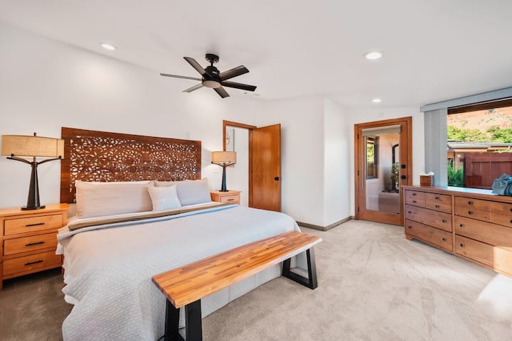 - Quarto com cabeceira de madeira esculpida e iluminação suave   - Ventilador de teto e tons neutros criam um refúgio tranquilo   - Banco de madeira adiciona charme e conveniência extra