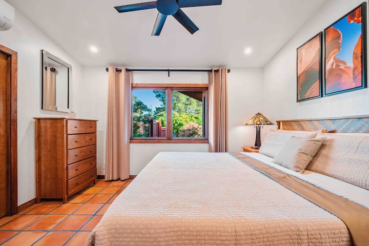 - Quarto aconchegante com cama king size e obras de arte do deserto   - Ventilador de teto e lâmpadas adicionam conforto e estilo   - Janela destaca a vegetação e as árvores ao redor