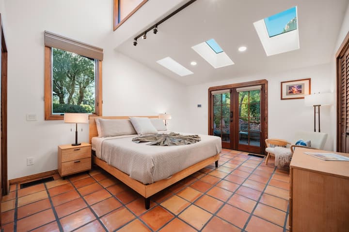 - Quarto com grande janela emoldurando o cenário de rocha vermelha   - Design minimalista com cômoda de madeira e obras de arte   - Espaço confortável com luz natural brilhante do deserto
