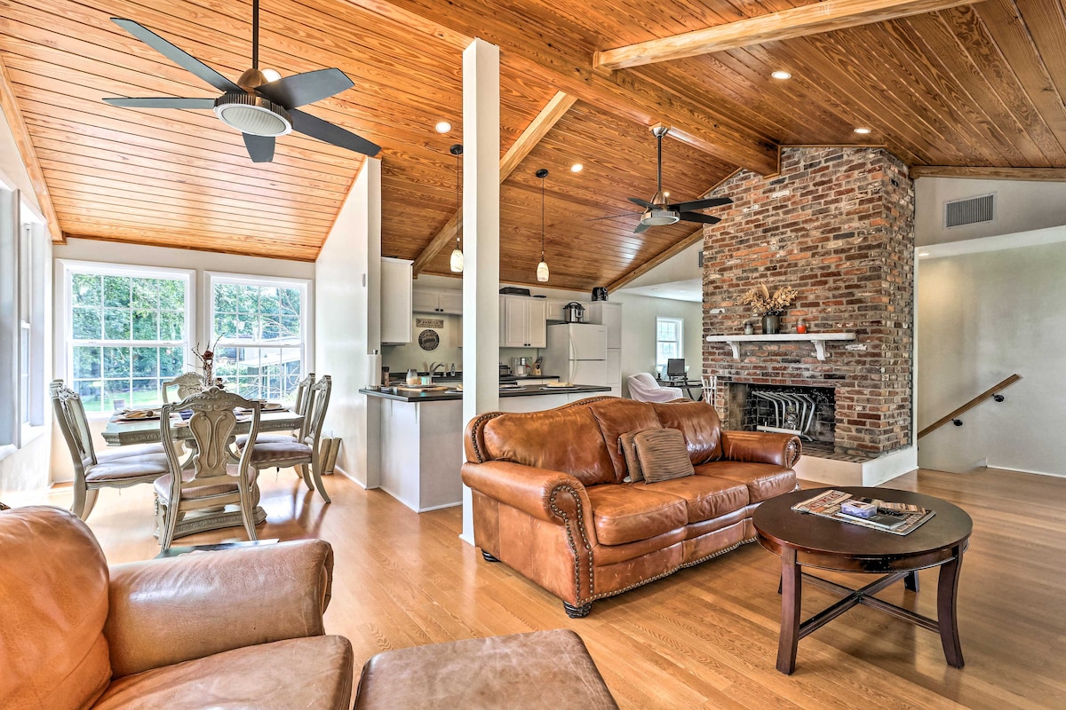 An open-concept living area features a cozy seating arrangement with leather sofas and a coffee table. The wood-beamed ceiling adds warmth, while large windows allow natural light to fill the space. A stone fireplace serves as a focal point, enhancing the home's inviting atmosphere.