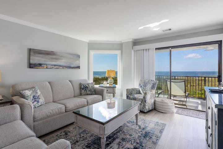 This beautifully furnished living room features sweeping ocean views framed by a large picture window and sliding glass doors that open to the private balcony.