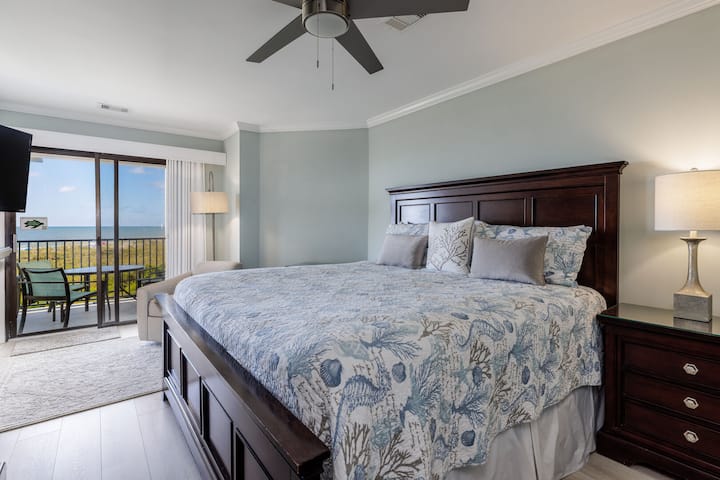 The serene primary bedroom offers a spacious retreat with a king bed, soft coastal décor, and abundant natural light.