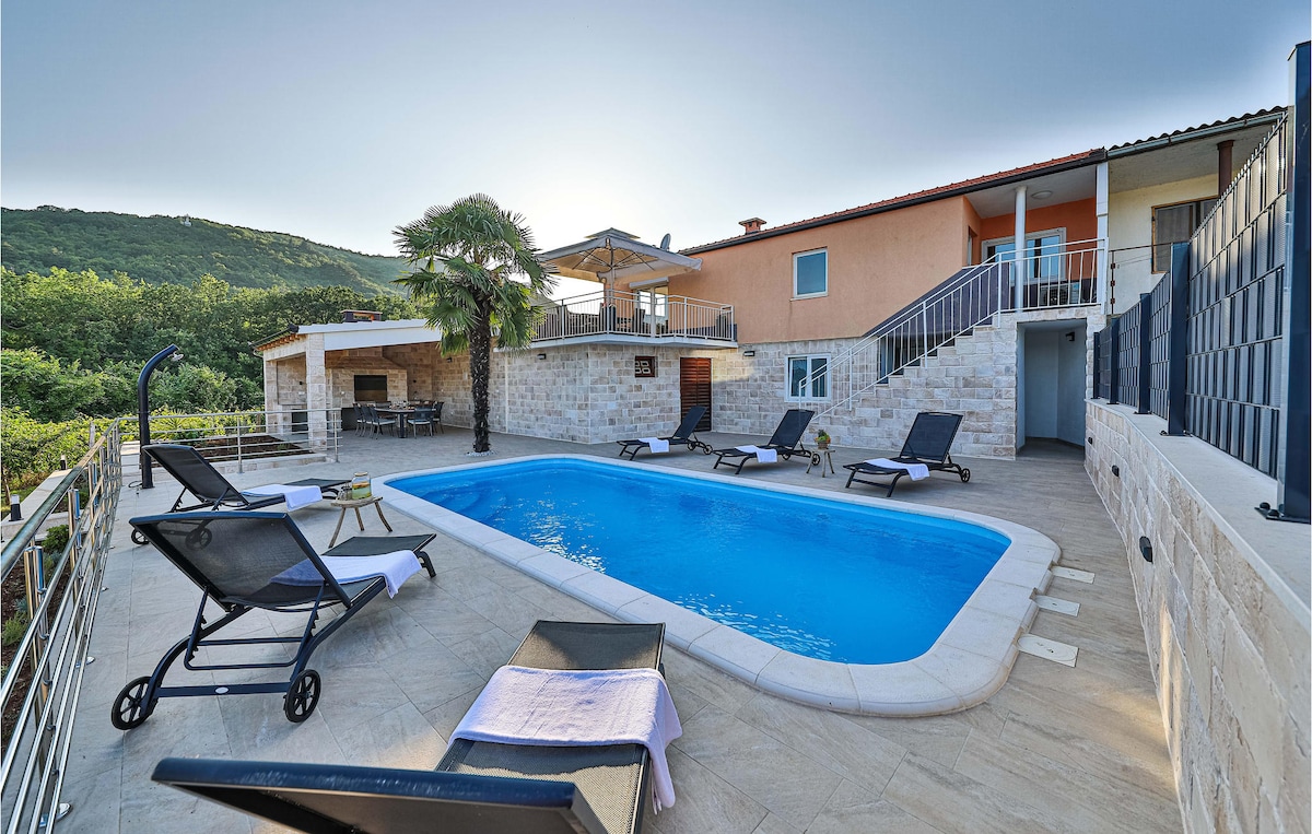 An outdoor area features a private swimming pool surrounded by sun loungers. A stone terrace offers access to the main house, which has two levels. Lush greenery and an outdoor dining space can be seen in the background, with a BBQ area nearby.
