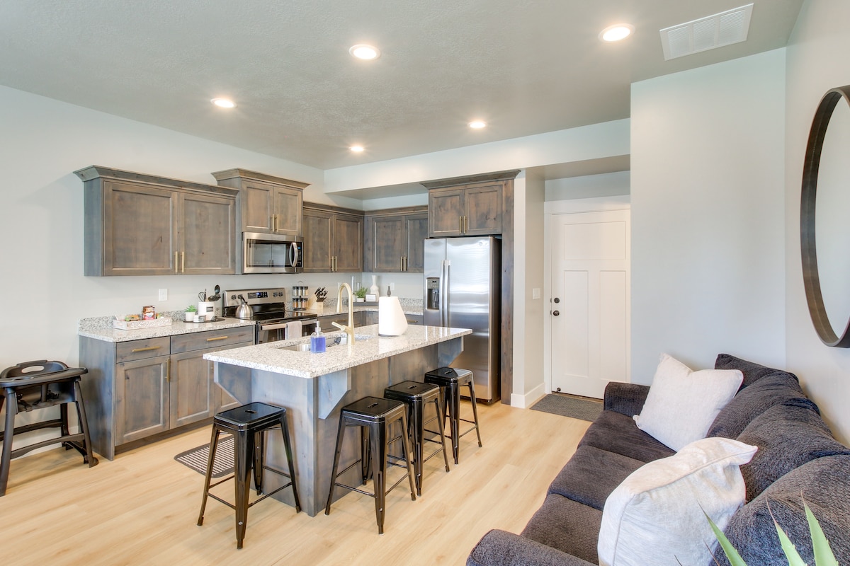 A modern kitchen boasts stainless steel appliances and ample counter space, with a large island featuring bar seating. The adjacent living area includes a comfortable dark sofa, creating an open-concept layout that promotes a welcoming environment.