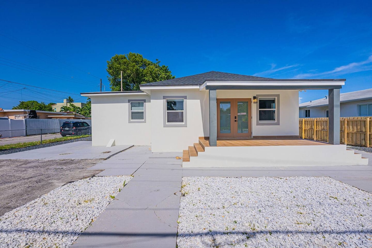 The exterior of the casita is showcased, featuring a modern facade with a combination of light-colored walls and a dark roof. A wooden deck leads to the entrance, and a gravel area surrounds the home, providing an open and welcoming appeal.