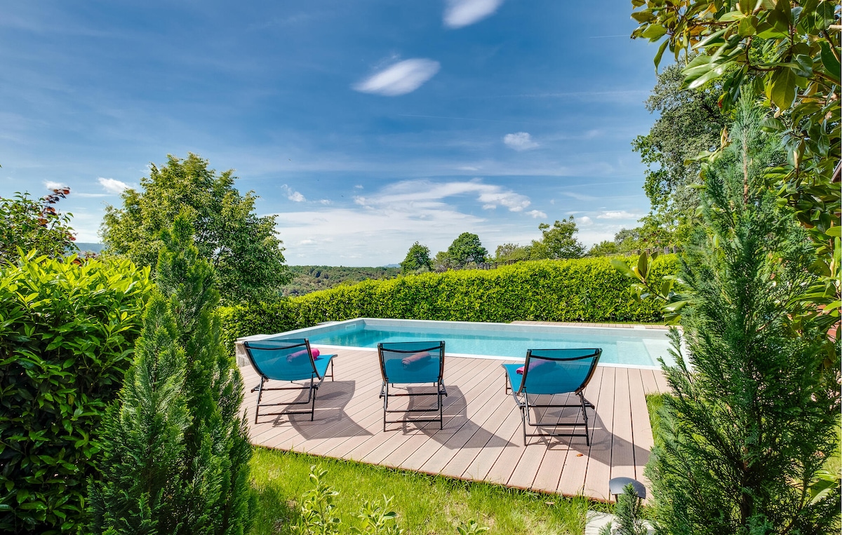 A tranquil outdoor scene features a private swimming pool bordered by a wooden deck. Three lounge chairs are positioned for relaxation, surrounded by lush greenery and shrubs, providing a peaceful retreat with scenic views of the countryside.