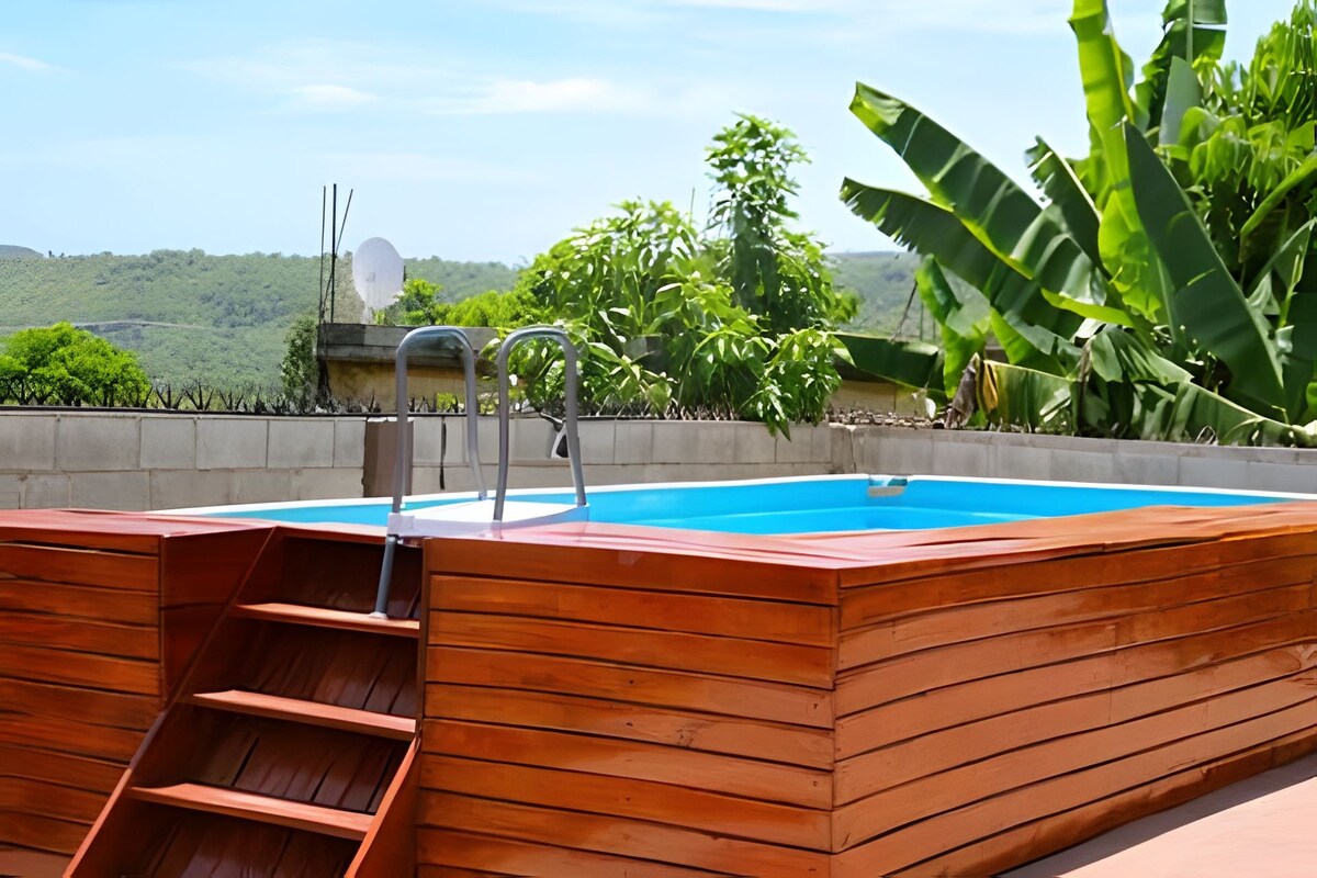A wooden deck surrounds a small private pool, complemented by a set of stairs leading into the water. Lush greenery, including banana plants, adds a tropical feel to the outdoor area, providing a serene setting for relaxation in nature.