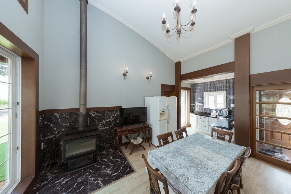 A dining area is presented with a large table surrounded by wooden chairs. A modern stove is situated in the corner alongside a well-equipped kitchen visible through an open doorway, offering a seamless flow between spaces.