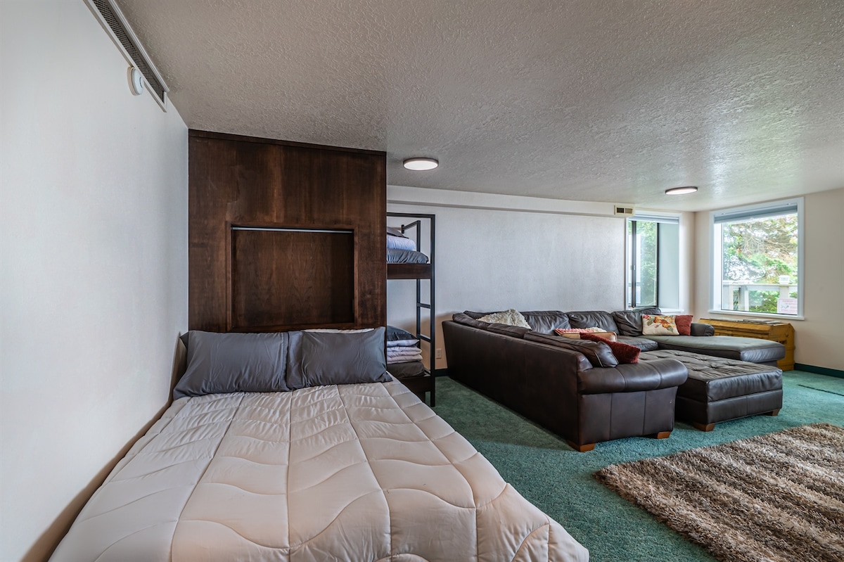 Habitación adicional con una cama completa y un juego de literas individuales, un sofá grande, un televisor, una mesa y una puerta a la terraza trasera.