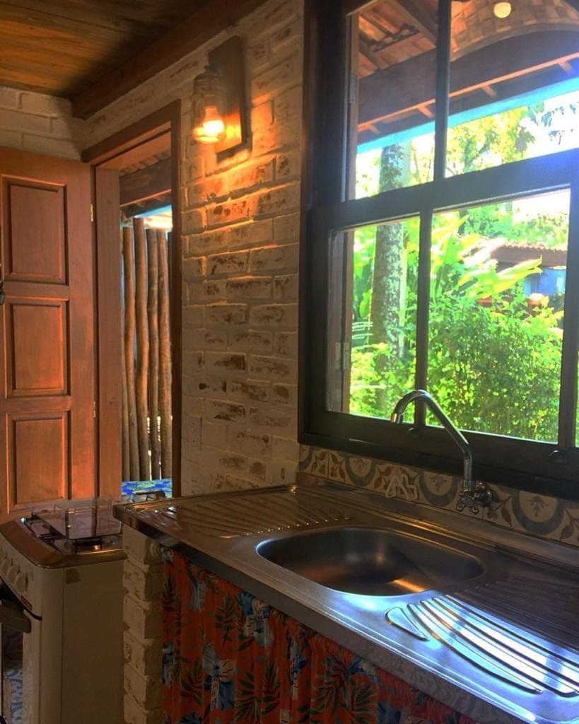 A well-equipped kitchen is presented, featuring a stainless steel sink and a stove. Natural light streams in through the large window, offering a view of the surrounding greenery. The space is complemented by a decorative curtain that adds a touch of color.