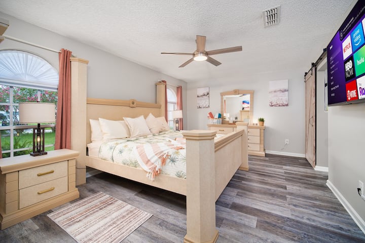 Amplio dormitorio con cama tamaño king, TV inteligente y grandes ventanales que ofrecen vistas al jardín.