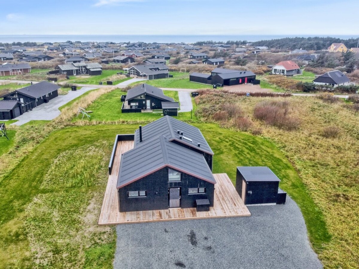 An aerial view captures a single-family house surrounded by natural landscapes. The property features a spacious wooden deck and is set against a backdrop of neighboring homes and greenery, offering a sense of openness and proximity to nature.
