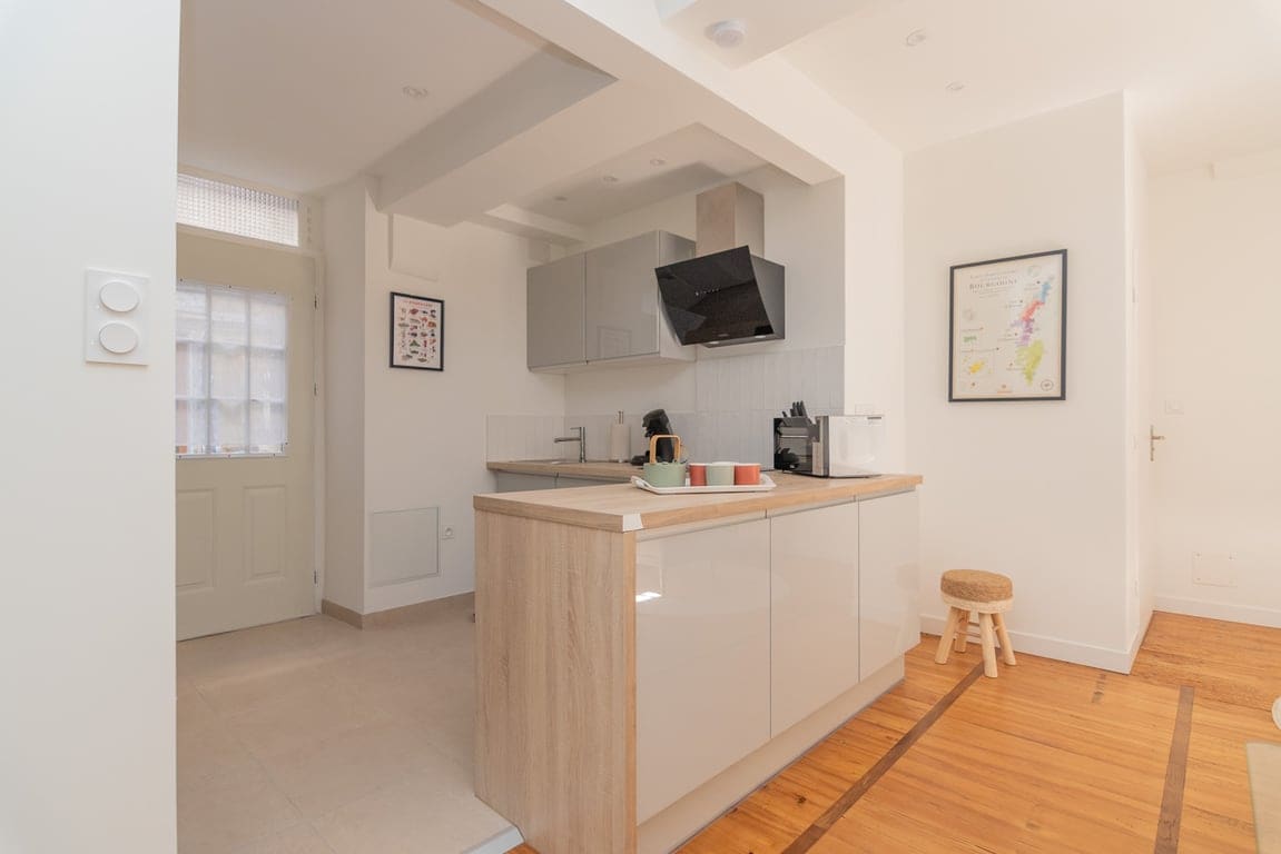 The kitchen features modern cabinets and a neutral color palette, with a stove and a microwave mounted above the countertop. Natural light enters through the entryway, illuminating the space. A small stool is positioned near the kitchen area, enhancing its functionality.