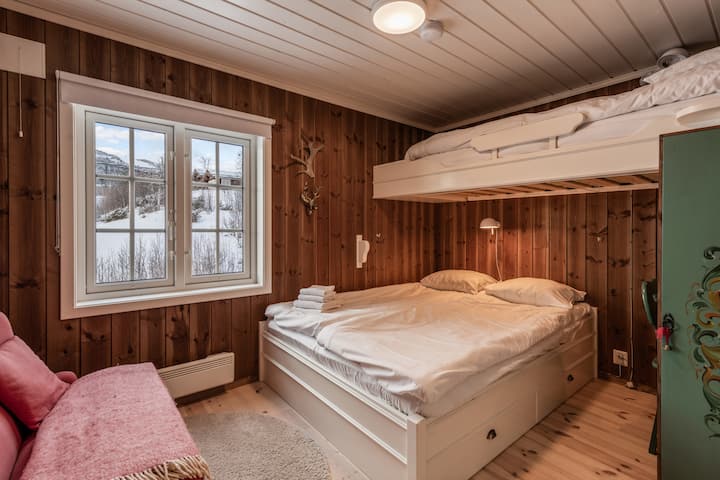Une chambre confortable avec des murs en bois, un lit double avec rangement, un lit superposé et une grande fenêtre avec vue sur une montagne enneigée.
