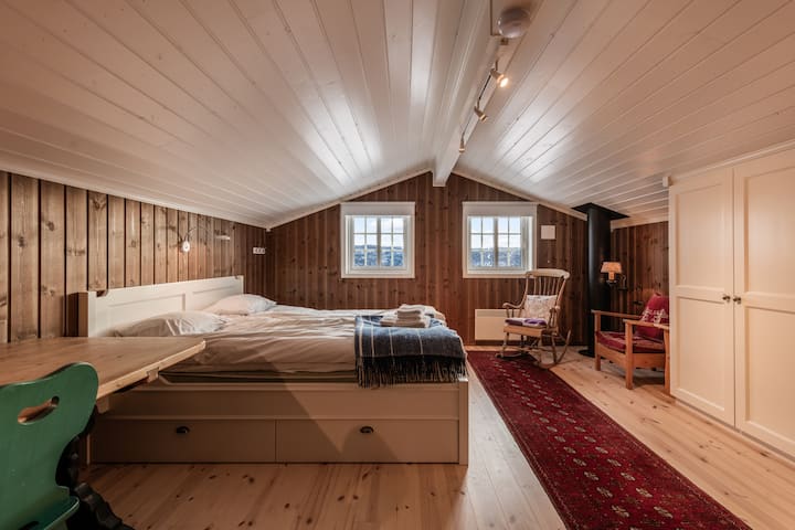 Une chambre spacieuse dans un grenier avec un lit double confortable et un espace de rangement intégré, ainsi qu'un coin salon charmant avec une chaise à bascule.