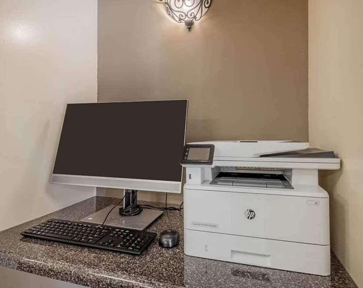 A dedicated workspace features a sleek computer monitor on a dark granite countertop, accompanied by a wireless keyboard. A multifunction printer sits adjacent, providing convenient access for various business needs. Soft overhead lighting creates an inviting environment for productivity.