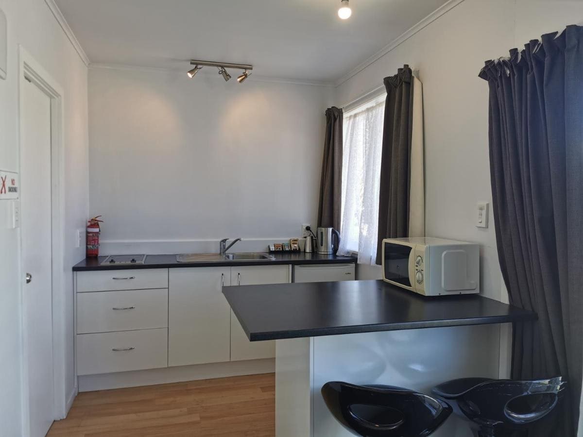 The kitchen area is characterized by modern cabinetry and a dark countertop. Essential appliances, including a kettle and microwave, are present. Natural light filters through a window, with curtains set to the side. A small table with two sleek chairs adds functionality to the space.