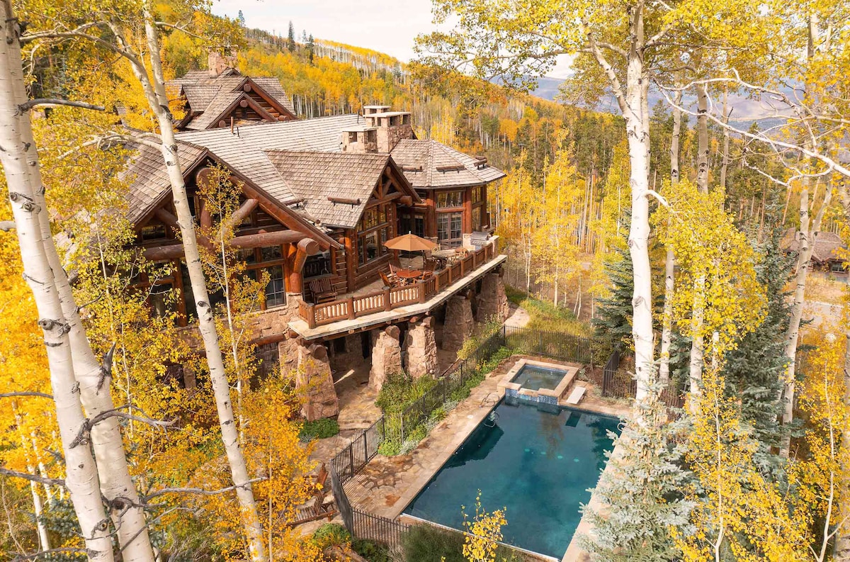 This luxury villa is nestled among vibrant autumn foliage, with a spacious outdoor area featuring a relaxing pool and a sun deck. The wood and stone construction harmonizes with the natural landscape, while expansive windows offer stunning views of the surrounding trees and mountains.
