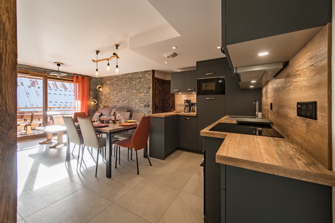 A modern kitchen area features sleek cabinetry with an open layout, complemented by a dining space that accommodates four. Large windows allow natural light to illuminate the room, enhancing the stone wall details. A warm wood countertop adds contrast to the contemporary design.